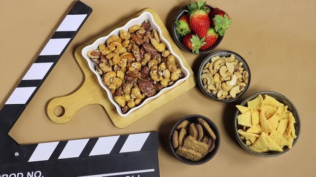 Clapperboard On Film Set Table With nuts, almonds cashews pecans and walnuts coated in smoky spiced caramel and Chips, and Strawberries, biscuit Casual Food Break On Set