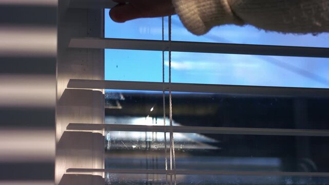 Hand closing window blinds in sunshine