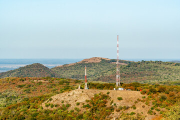 Obraz premium Communication towers on a hilltop surrounded by green hills and clear sky in an open landscape during the day