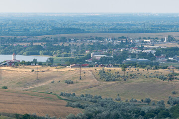 Obraz premium View of a small town by a river surrounded by fields and hills during a clear day in summertime