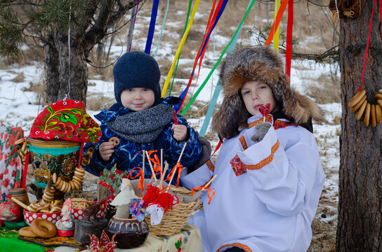 Carnival in Russia: two children at the samovar with ribbons, in winter clothes and a Russian shirt. Folk traditions.