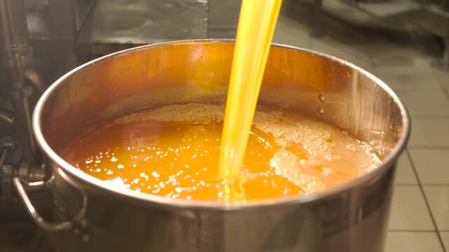 Industrial process of pouring orange juice concentrate into a stainless steel tank. Manufacturing of sweet fruit beverages at a food factory.