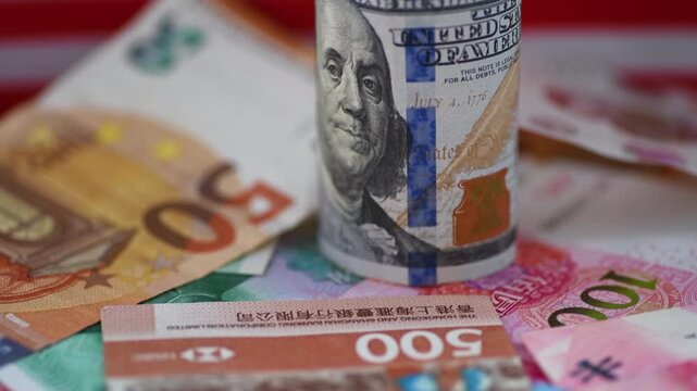 A macro close up of a roll of US dollar bills on top of other currency bank notes with the flag of United States of America in the background. A dollar hegemony concept.