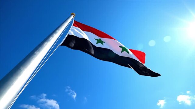 Syrian flag waving on a silver pole against a clear blue sky with sunlight shining through the clouds