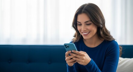 Fototapeta premium Woman sitting on couch smiling while using her smartphone