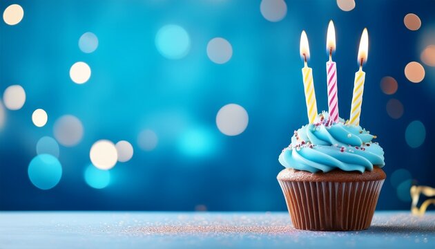 birthday cupcake with 3 candles on blured blue background with big empty copyspace
