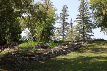 Fototapeta premium stone steps (stairs) lined with boulders, quarried stone, landscaped lawns, shady boreal forest trees (wide-angle, panorama, landscape, summer, sunshine)