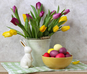 Easter celebration with vibrant colored tulips bouquet, decorative bunny figurine, and dyed eggs symbolizing spring arrival and holiday tradition