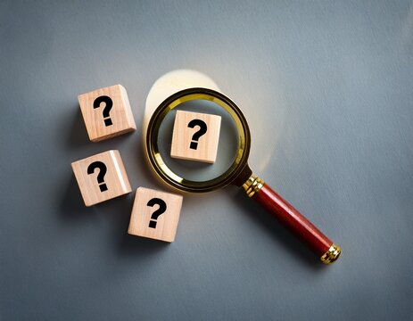 identifying and understanding issues through root cause analysis using a magnifying glass on wooden cubes with question marks on a grey background