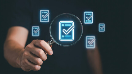 Hand holding magnifying glass focusing on a digital checklist symbol representing quality control evaluation and attention