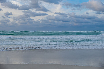 Obraz premium Waves crash on the shore under a cloudy sky at twilight on a beach