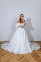 Fototapeta premium Portrait of a beautiful bride in a white luxurious long and lush dress. Wedding salon, clothes fitting
