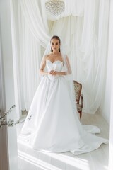 Portrait of a bride in a white lush luxury dress with pearls. Dress fitting before the wedding