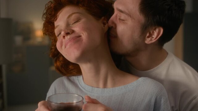 Cinematic close up shot of authentic young couple sharing slow morning together with man kissing girlfriend on neck gently, copy space