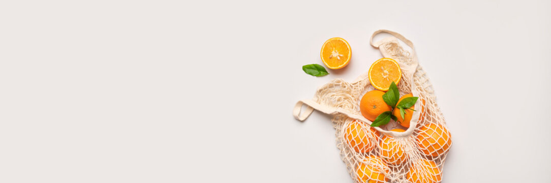 Mesh string bag with ripe oranges on gray background flat lay top view. Concept of reusable bag for shopping, goods, and eco-friendly living. Zero waste. Background with citrus fruits