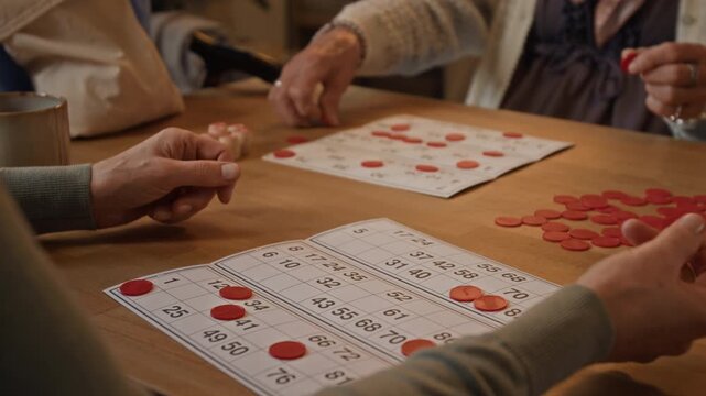 Low angle close-up shot of unrecognizable seniors marking numbers while playing bingo at table in retirement home