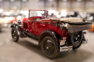 Classic red convertible car parked indoors during a vintage automobile show with various cars in the background on a bright day