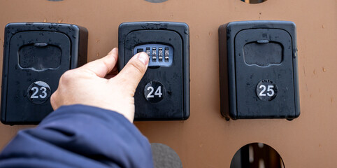 Close-up of fingers dialing a numeric code on a rental property lockbox, illustrating self check-in...