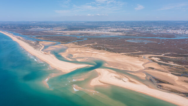 Aerial view shows Ria Formosa and Praia de Faro with sandy shores and clear water. The landscape highlights the natural beauty of the region in Portugal