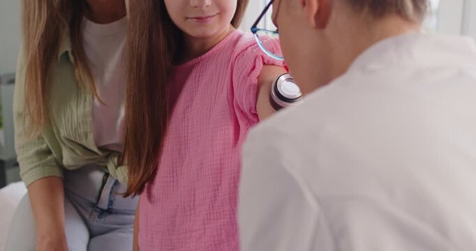Pediatric dermatologist using dermatoscope for arm skin exam of child during routine checkup in hospital. Kid patient and mother visit doctor to check mole and skin health during clinic appointment