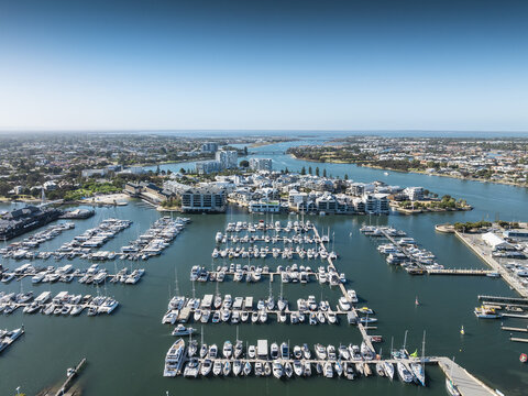 Aerial view of boats nestled in the marina's embrace, where turquoise waters meet the city's edge, framed by buildings and distant horizons, Mandurah, Western Australia, Australia.