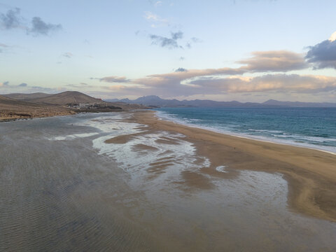 Aerial view of the coastline where the golden sandy beach meet the turquoise waters under a sunset sky, Jand&Atilde;&shy;a Natural Park, Fuerteventura, Canary Islands, Spain.