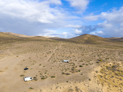 Aerial view of arid, undulating terrain dotted with sparse vegetation and scattered vehicles under a vast sky in Jand&Atilde;&shy;a Natural Park, Jand&Atilde;&shy;a Natural Park, Canary Islands, Spain.