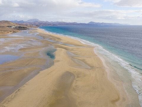 Aerial view of the turquoise sea meeting the golden sands of Jand&Atilde;&shy;a Natural Park under a vast sky, Jand&Atilde;&shy;a Natural Park, Fuerteventura, Canary Islands, Spain.