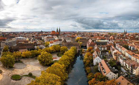 Aerial view of the Pegnitz River winding through the city, lined by trees in golden autumn foliage, with the imposing St. Lorenz church in the distance, Nuremberg, Germany.
