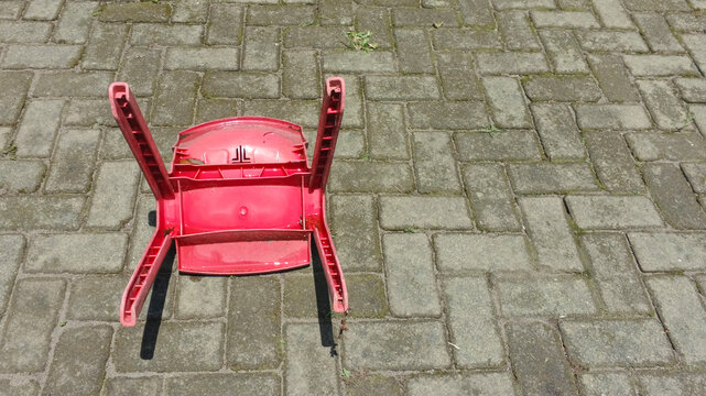 Close up of a broken and overturned red plastic chair in the yard. Copy space for text. For graphic design, 3D rendering and banners