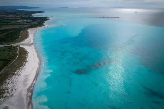 Aerial view of the mesmerizing turquoise sea meeting the sandy beach near the Solvay plant's industrial pier, Rosignano Solvay, Tuscany, Italy.