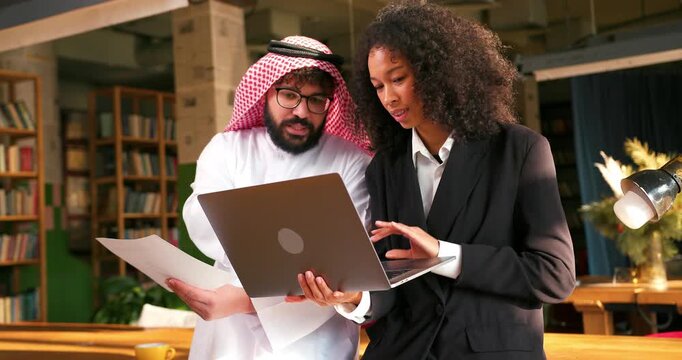 Confident muslim man wearing keffiyeh and hispanic woman using laptop analyzing planning project