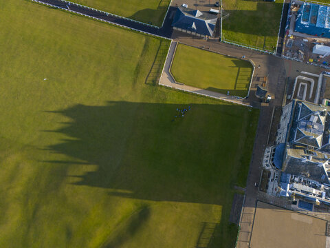 Aerial view of crisp, verdant fairways meeting the architectural lines of nearby buildings under the long shadows of late afternoon, St Andrews, United Kingdom.