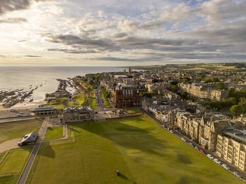 Aerial view of the iconic Old Course at St Andrews basking in the warm glow of the setting sun, a tapestry of green fairways meeting the rugged coastline, St Andrews, Scotland, United Kingdom.
