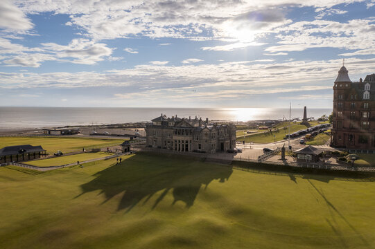 Aerial view of the iconic Royal and Ancient Golf Club of St Andrews basking in the sunlight, its shadow stretching across the lush green landscape, St Andrews, Scotland, United Kingdom.