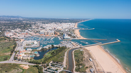 Obraz premium The marina in Vilamoura, Algarve, Portugal. Boats are lined up at the docks with the beach and cityscape in the background under blue skies. Aerial