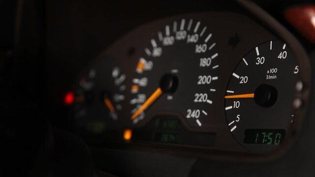 Close up view of a car dashboard instrument cluster focusing on the tachometer with the needle moving up and down as the engine revs, speedometer visible in background.

