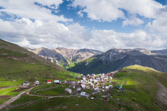 Aerial view of rustic rooftops nestled in vibrant green hills, contrasting with the rugged, towering mountains, Lukomir, Federation of Bosnia and Herzegovina, Bosnia and Herzegovina.