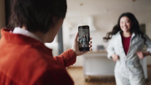 Man filming Asian girlfriend dancing on phone camera for social media content