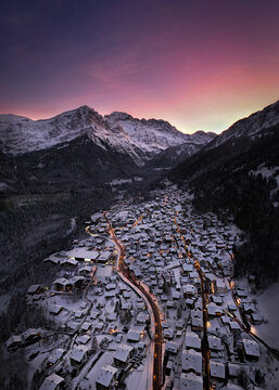 Aerial view of a snow-laden village nestled between towering, snow-capped mountains under a vibrant, colorful sky, Champ&Atilde;&copy;ry, Valais, Switzerland.