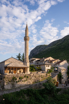 Aerial view of the Karadoz Bey Mosque stands majestically, its minaret piercing the sky above the old stone buildings, framed by a rugged mountain backdrop, Mostar, Bosnia and Herzegovina.