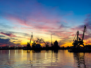 Obraz premium Sunset over the harbor with cranes and buildings silhouetted against the colorful sky