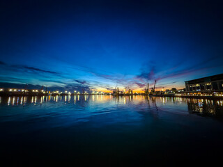 Obraz premium Sunset over the harbor with boats and cranes in the water reflecting colors
