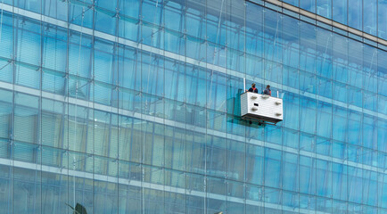 Professional Window Cleaners on Modern Glass Skyscraper Facade in Maintenance Cradle High Rise Building Infrastructure and Architecture