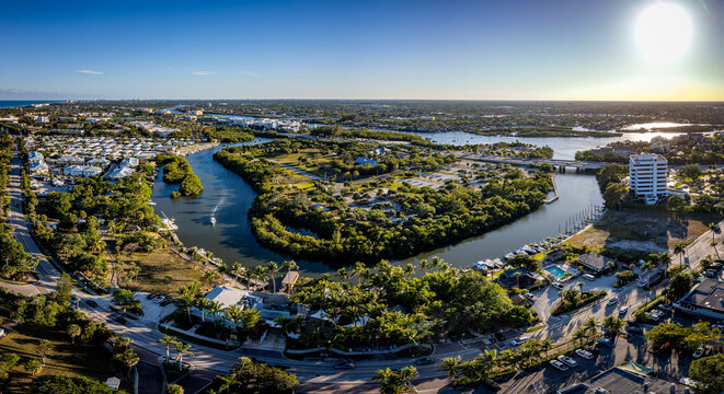 Aerial view of the Loxahatchee River curving through lush greenery and buildings under a bright sun, Jupiter, Florida, United States.
