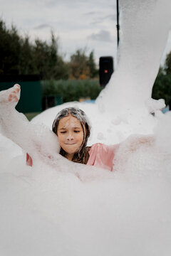 A joyful child laughs and plays in bubbly foam outdoors during golden hour with trees and soft light around