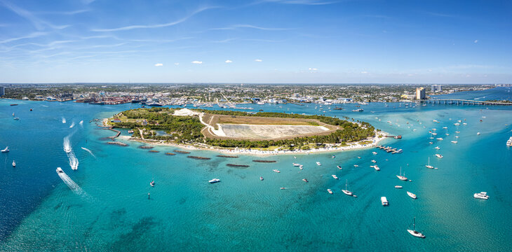Aerial view of boats dot the turquoise waters surrounding Peanut Island, a vibrant oasis contrasting with the distant cityscape, Peanut Island, Florida, United States.