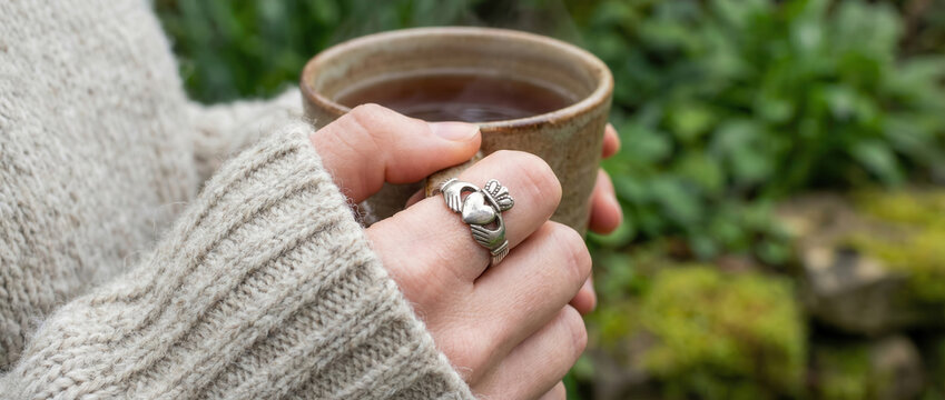 Woman wearing irish claddagh ring and holding hot drink in a mug. Holiday traditions and celtic culture. St. Patricks Day celebration.