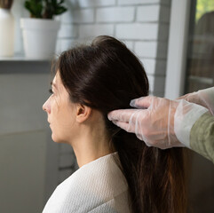 Naklejka premium Gloved hands carefully section a womans long dark hair. bright room with plants beauty salon preparation hair care concept