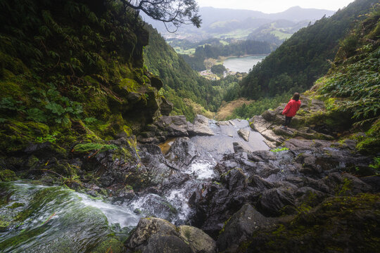 Aerial view of a waterfall cascading down moss-covered rocks, with a glimpse of a distant lake and lush green landscape, S&Atilde;&pound;o Miguel, Coimbra, Portugal.